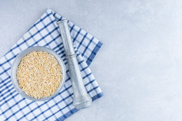 Folded towel underneath a herb masher and a metal jug of brown rice on marble surface