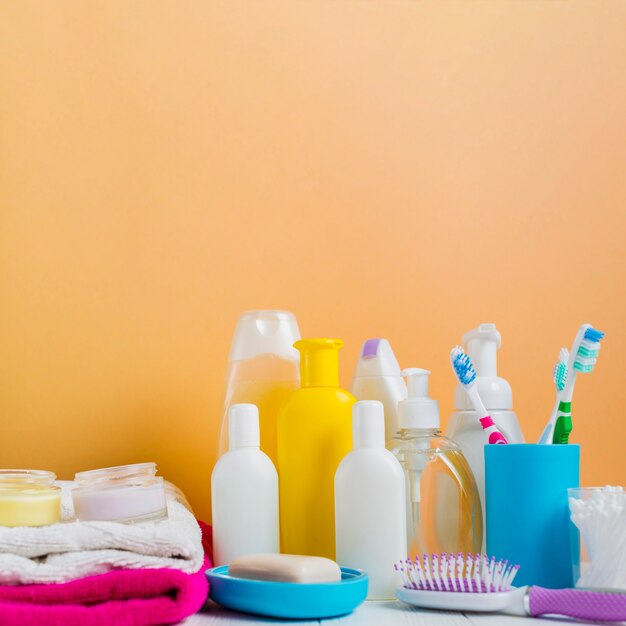 Folded towel with cosmetics products and toothbrushes against an orange background