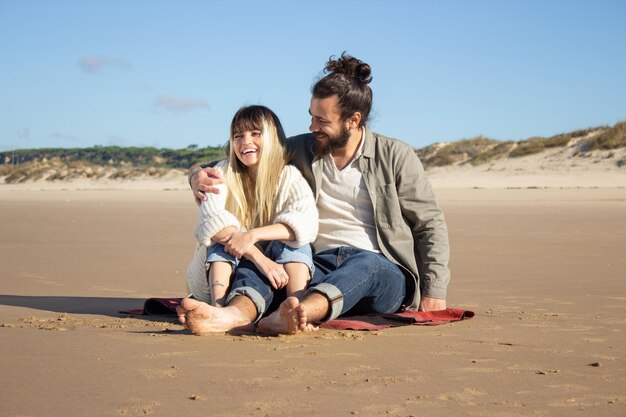 Fond Caucasian couple on summer vacation. Bearded man and woman in casual clothes sitting on blanket, hugging on shoulder. Love, travelling, tenderness concept