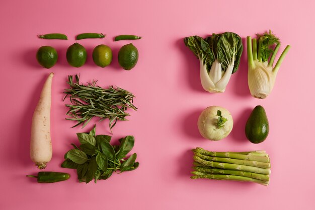 Еда и свежие овощи. зеленая спаржа, лайм, авокадо, белый редис, rosemay, базилик, изолированные на розовой поверхности. продукты или ингредиенты для приготовления здоровых блюд из органических продуктов. диета, сельское хозяйство