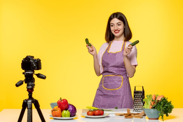 Food blogger cute lovely chef in pink apron recording video for social media holding cucumbers