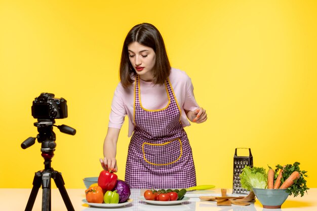 Food blogger young girl in pink apron recording video for social media reaching to pepper
