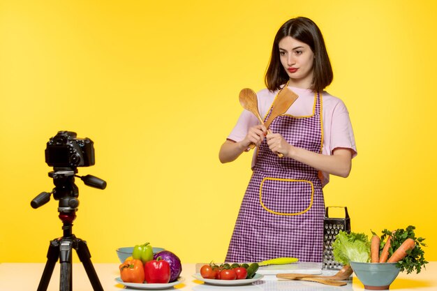 Food blogger young girl in pink apron recording video for social media with wooden spoons
