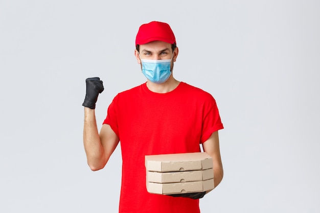 Food delivery, application, online grocery, contactless shopping and covid-19 concept. Fast and safe delivery, champions in industry. Courier in red uniform fist pump, deliver pizza order