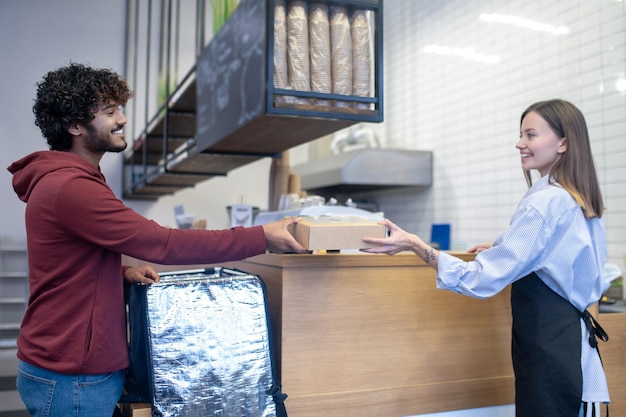 Foto gratuita consegna del cibo. giovane corriere dai capelli ricci che prende la scatola del pasto per la consegna