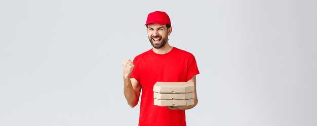 食品配達検疫は家にいてオンラインコンセプトを注文する赤いTシャツと帽子の熱狂的な宅配便はピザの注文を家の拳ポンプにもたらします自信を持って勝利を祝う勝利