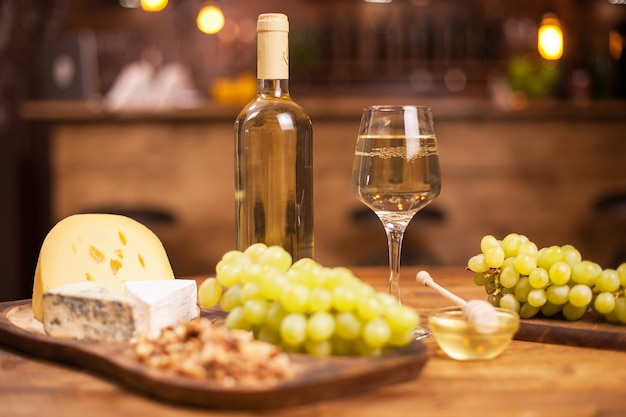 빈티지 레스토랑에서 다양한 치즈와 화이트 와인이 있는 음식 축제. 화이트 와인 한 병입니다. 신선한 포도입니다.