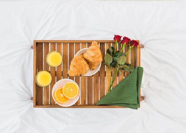Food and flowers on breakfast table on bed sheet