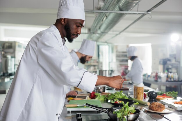 Food industry expert adding fresh green herbs to improve dish taste. Gastronomy expert wearing cooking uniform while preparing delicious gourmet dish for dinner service at restaurant.