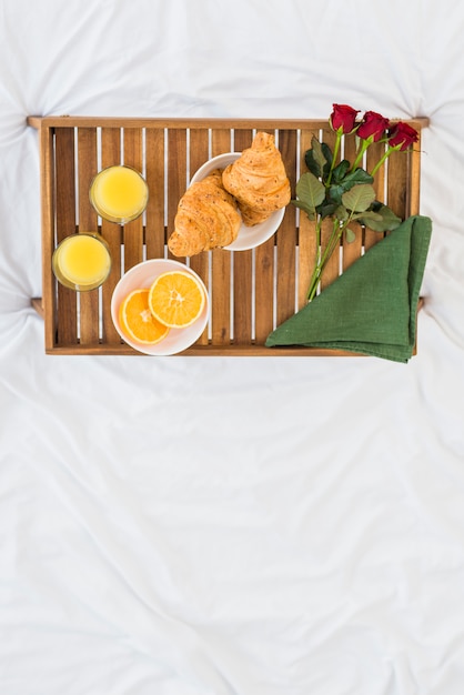 Food and roses on breakfast table on bed sheet 