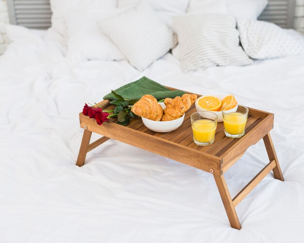 Food and roses on breakfast table on bed