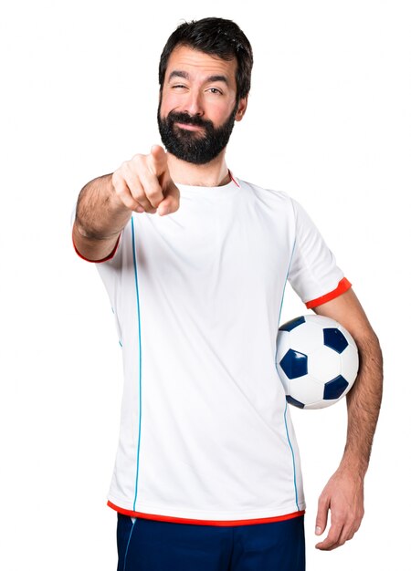 Футболист с футбольным мячом, указывающим на фронт