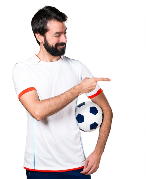 Free photo football player holding a soccer ball pointing to the lateral