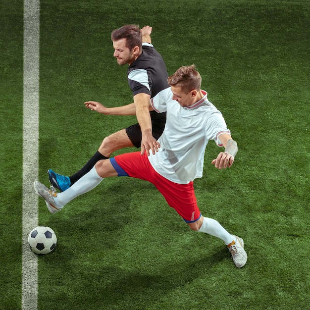 Free photo football player tackling for ball over green grass wall. professional male soccer players in motion at stadium. fit jumping men in action, jump, movement at game.