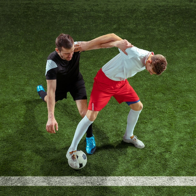 緑の芝生の壁を越えてボールに取り組むフットボール選手。スタジアムで動いているプロの男子サッカー選手。ジャンプする男性をアクション、ジャンプ、ゲームでの動きに合わせます。