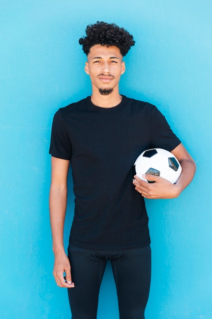 Football player with ball under arm near wall