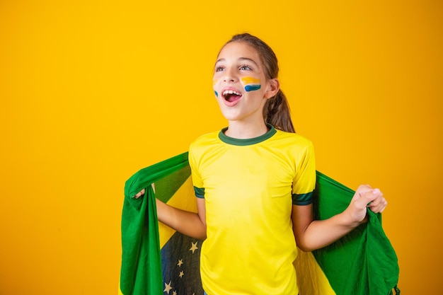 サッカーサポーター、ブラジルチーム。黄色の背景で彼女のチームを応援して美しい少女
