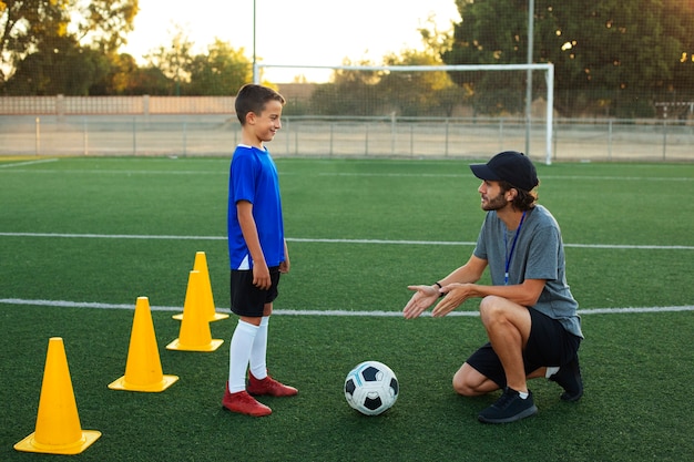 Foto gratuita allenatore di calcio che insegna la vista laterale del bambino