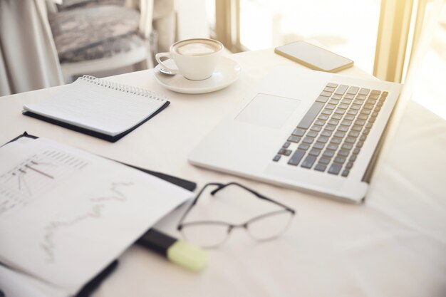Foreground of objects on the working place: eyeglasses, diagrammes, laptop, notebook