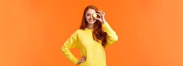 Forget about diet lets enjoy cheerful and happy smiling redhead woman holding small tasty macaron ov