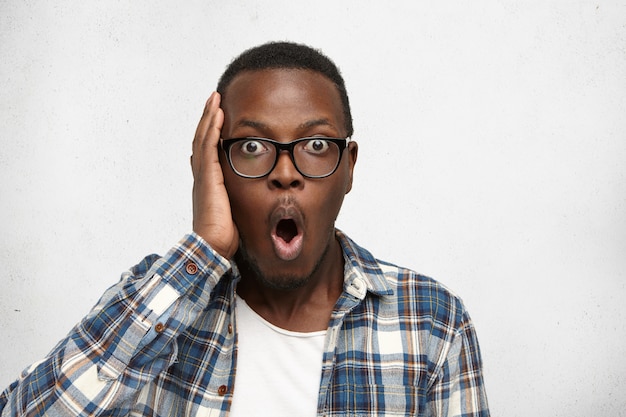 Free photo forgetful afro-american student in stylish glasses holding hand on head staring with astonished amazed look, having completely forgotten about serious examination at college.