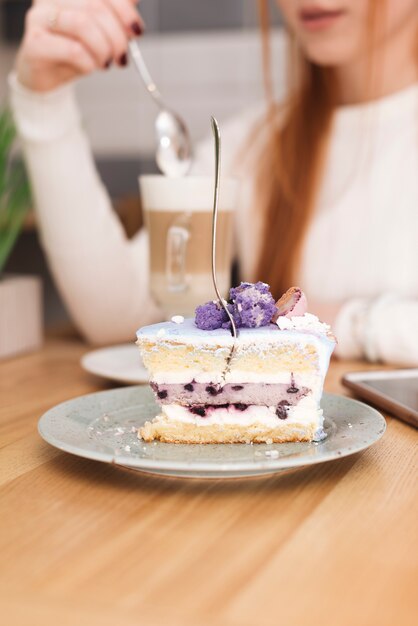 라떼 마끼아또가 든 여성 앞에서 맛있는 레이어 케이크 조각에 포크 삽입