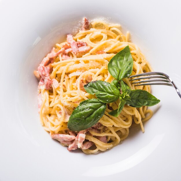 Fork over the spaghetti with meat and basil leaf on plate