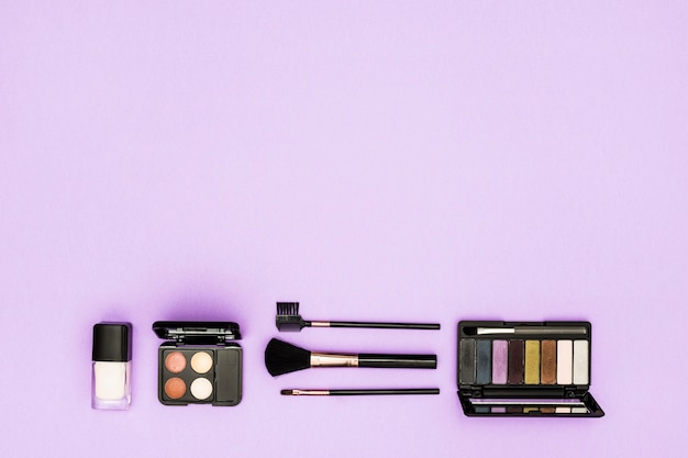 Free photo foundation bottle; eyeshadow palette and makeup brushes on purple background