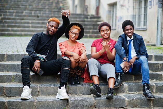 Четыре африканских друга веселятся на свежем воздухе Две черные девушки с парнями сидят на лестнице старого города