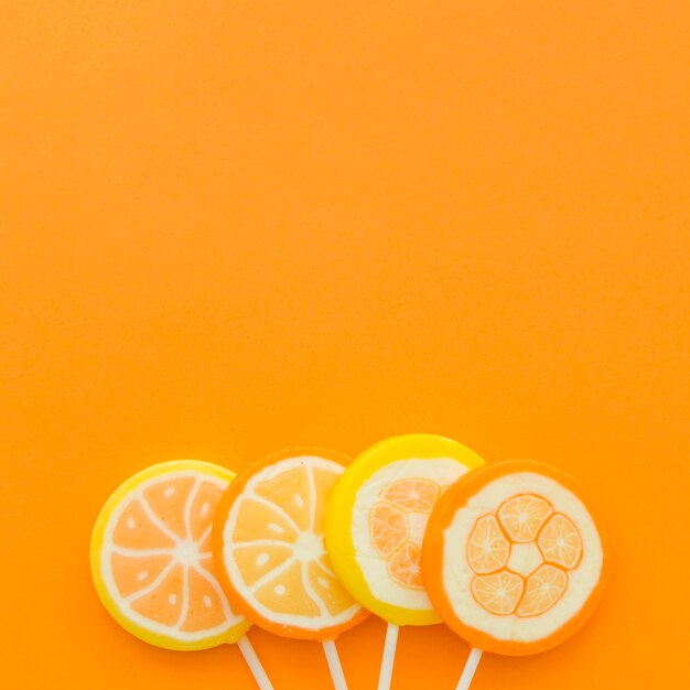 Four citrus fruit lollipops at the bottom of orange backdrop