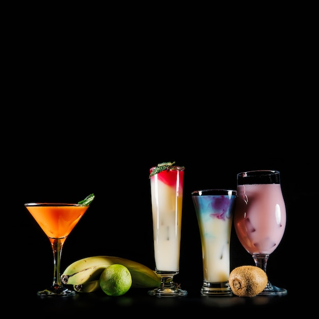 Four cocktails and exotic fruits on black background