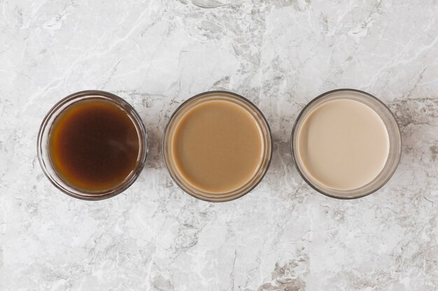 Четыре чашки кофе в ряд на мраморном фоне с различными смесями молока и кофе