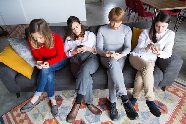 Four colleagues sitting on couch and using cellphones