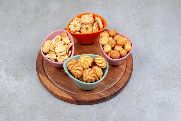 Four colorful bowls of crispy biscuits and cookie chips on wooden board on marble background. High quality photo