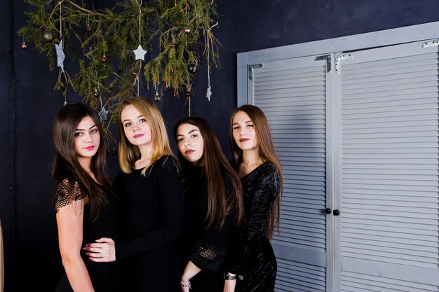 4人のかわいい友達の女の子がクリスマスの飾りに対して黒いドレスを着ています