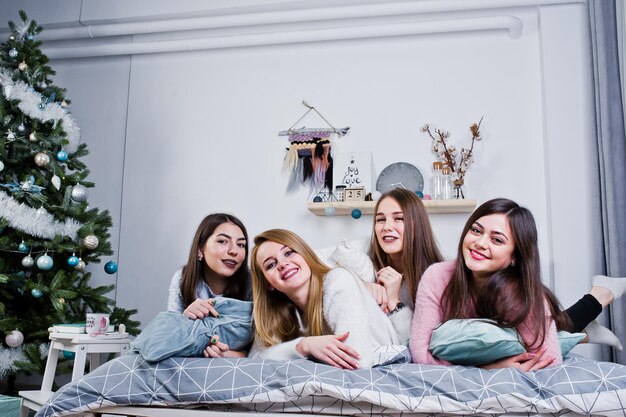4人のかわいい友達の女の子が暖かいセーターと黒いズボンを着て、枕でスタジオで遊ぶ新年の装飾が施された部屋で