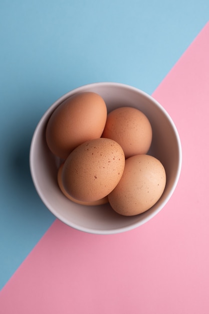 Four eggs in a bowl on a blue and pink surface
