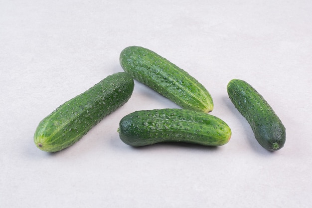 Four fresh cucumbers on white surface