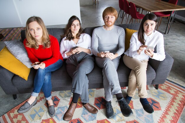 Four friends posing on couch with smartphones in hands