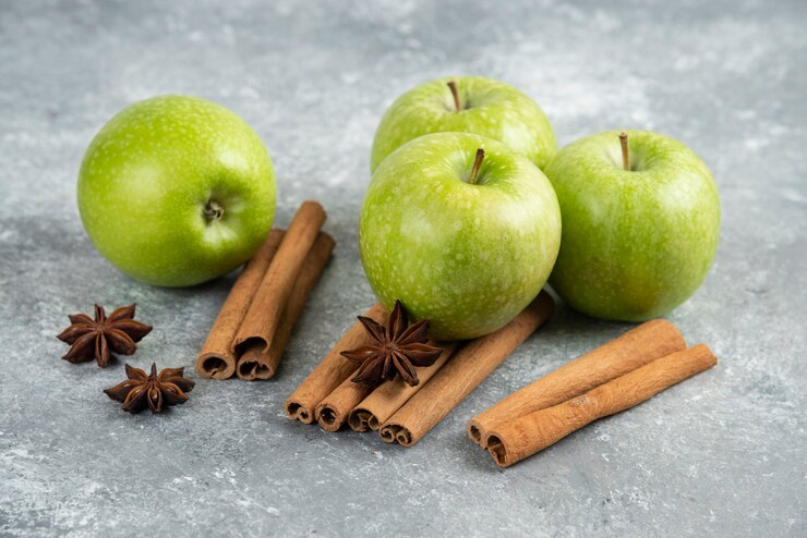 Free Photo four green apple and cinnamon sticks on marble table.