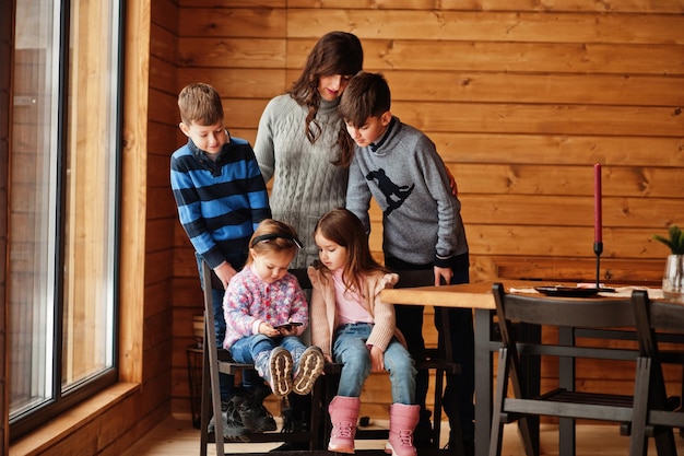 Four kids with mother in modern wooden house watching video in mobile phone