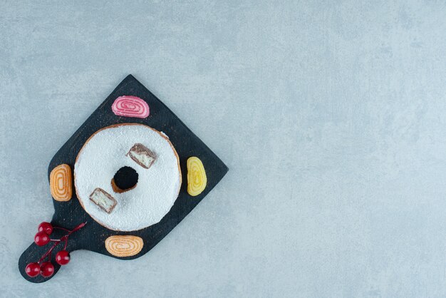 Four marmelades and a donut on a black board on marble.