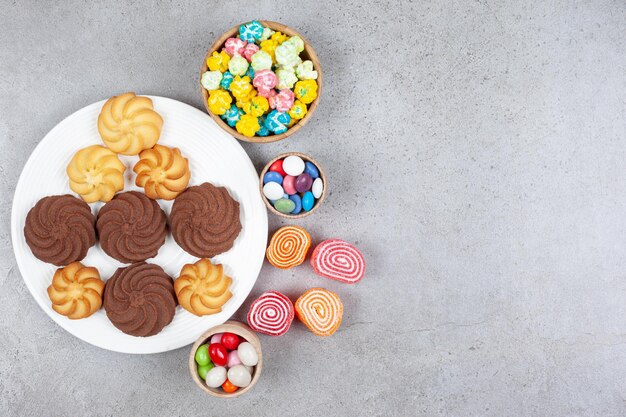 Four marmelades, three bowls of candy and a plate of assorted cookies on marble background. High quality photo