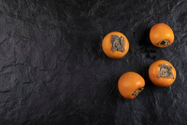 Four ripe persimmon fruit placed on black surface