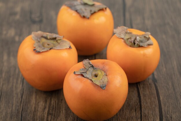 Four ripe persimmon fruits placed on wooden surface