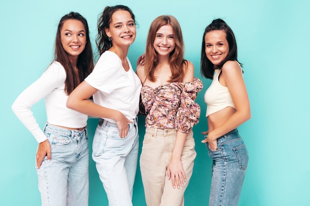 최신 유행의 여름 옷을 입은 4명의 젊고 아름다운 웃는 갈색 머리 힙스터 여성 파란색 벽 근처에서 포즈를 취하는 섹시하고 평온한 여성 긍정적인 모델 재미 명랑하고 행복한