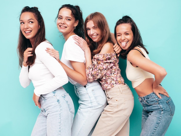 Four young beautiful smiling brunette hipster female in trendy summer clothes Sexy carefree women posing near blue wall Positive models having fun Cheerful and happy