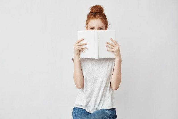 foxy woman hiding face behind book.