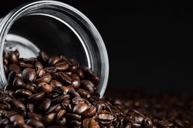 Fragrant coffee beans are scattered from a jar on a rustic tabletop background Closeup selective focus Copy space banner