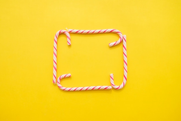 Frame of candy canes on yellow background